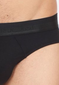 Schwarze Unterhosen mit einem weichen, elastischen Bund, der ein erhabenes Logo trägt. Glattes Baumwollmaterial mit einem körpernahen, tief sitzenden Design.