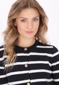 Cardigan a righe navy e bianche con collo rotondo e bottoni dorati, caratterizzato da una texture morbida e un design aderente.