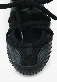 Nærbillede af sort sneakers tå med tekstureret strikstof, gummieret prikket såle kant og bindet sorte snørebånd på hvid baggrund.