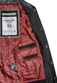 Black outer fabric lightweight jacket with red satin lining, featuring a size tag, care label, and two inner pocket slots. Brand label visible.