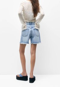 Shorts di denim azzurro con orlo sfrangiato, vita alta e tasche frontali, abbinati a sandali platform neri con cinturini blu.