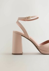 Sandale à talon bloc rose nude avec bride à la cheville et boucle dorée, présentant un talon large et une finition en cuir lisse.