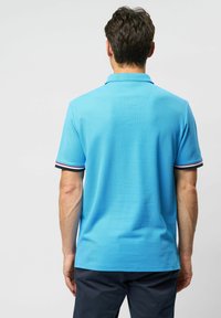 Lyseblå polo t-shirt lavet af tekstureret stof med krave og korte ærmer, prydet med sorte, røde og hvide stribede detaljer.