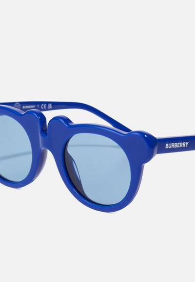 Modre sončne očala z zaobljenimi lečami in okvirjem v obliki medveda. Narejena so iz plastike, s modrimi lečami in logotipom "BURBERRY" na roki.