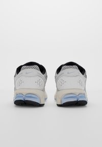 Un par de zapatillas de running Nike blancas y azul claro vistas desde atrás, mostrando el talón texturizado y las suelas negras sobre un fondo blanco.