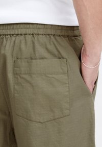 Olivirohelised lühikesed püksid, millel on tekstuuriga pind, elastne vöökoht ja üks tagatasku, millel on õmmeldud äärekate.