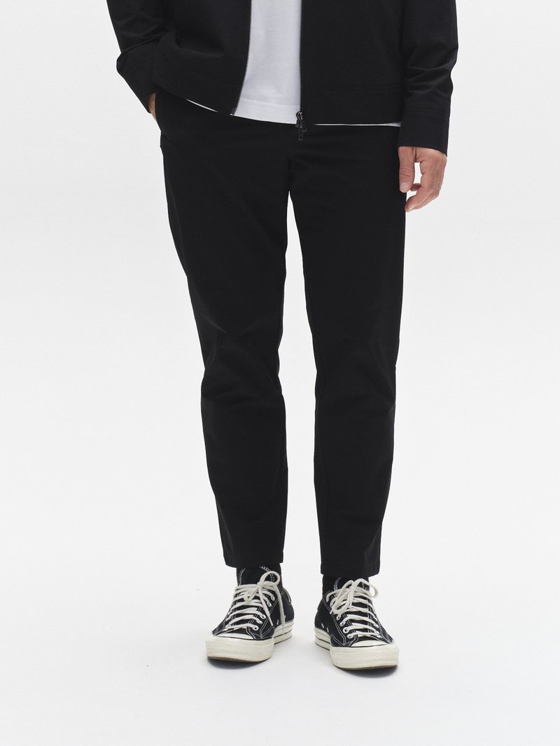 Černé kalhoty se zužujícími nohavicemi z lehké látky, doplněné černými plátěnými teniskami. Bunda má zipové zapínání a hladký povrch.