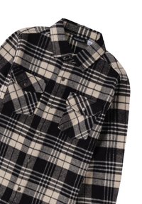 Camicia in flanella a quadri bianco e nero con colletto button-down, due tasche sul petto e bottoni a pressione in metallo. Texture morbida e materiale caldo.