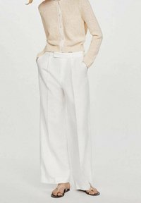 Białe spodnie o szerokich nogawkach z wysokim stanem, marszczonym przodem i kieszeniami po bokach, zestawione z beżowym, dzianinowym topem z guzikami.