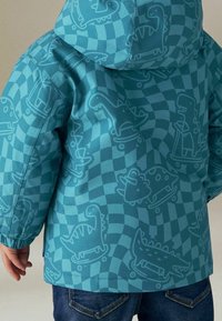 Giacca per bambini color teal con stampa di dinosauro su sfondo a scacchi. Realizzata in materiale morbido con polsini elasticizzati e cappuccio.