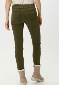 Jeans ajustados de color verde oliva, hechos de un tejido suave, con bolsillos traseros y una sutil costura decorativa en la cintura.