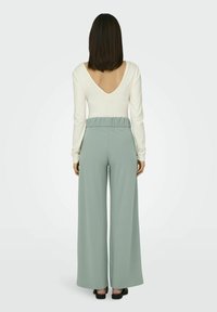 Dlhý rukáv, top s výstrihom do V v off-white farbe; nohavice so zvýšeným pásom a širokými nohavicami v jemne zelenej farbe s elastickým pásom a hladkou textúrou.