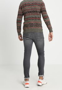Grau gemusterter Pullover mit roten Akzenten, kombiniert mit grauen Skinny-Jeans und weißen Sneakers mit orangefarbenen Details. Lässiges Outfit.