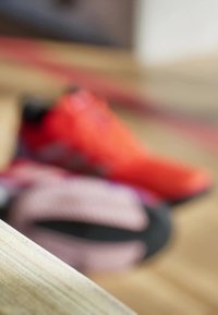 Running shoes in bright orange, featuring mesh material, a textured sole, and contrasting black accents. Out of focus background elements.