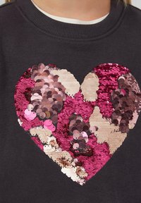 Dunkelgrauer Sweatshirt mit einem großen Herz aus glänzenden pinken und beigen Pailletten, das eine strukturierte und reflektierende Oberfläche aufweist.