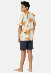 Camicia a maniche corte beige con motivo di palme arancioni, abbinata a pantaloni corti blu navy. Tessuto in cotone, vestibilità comoda e design casual.