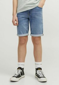 Vaaleansiniset farkkushortsit, joissa on käännetyt lahkeet ja etutaskut, käytettynä mustien korkeavartisten tennareiden ja valkoisten sukien kanssa, joissa on tekstiä.