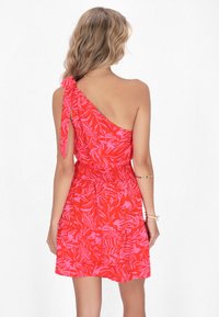 Rochie roșie cu o singură umăr, cu un model floral, talie strânsă și accesoriu legat pe umăr. Material ușor, cu o potrivire lejeră.