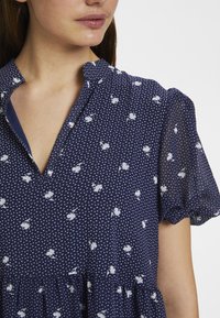 Abito blu navy con motivi floreali bianchi e pois. Presenta un colletto e maniche corte a sbuffo con un orlo a strati.