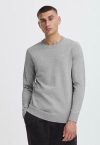 Gray knitted sweater with a round neck, ribbed cuffs, and hem. The fabric appears soft with a subtle texture, paired with dark corduroy pants.
