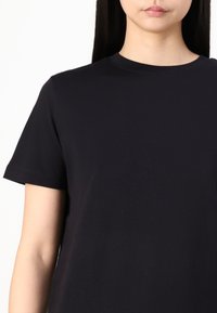 Black cotton t-shirt with a round neckline and short sleeves, featuring a smooth texture and a structured fit, showing a small portion of the torso.