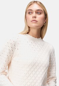 Helle cremefarbene Strickjacke mit einem Rautenmuster, geripptem Rundhalsausschnitt und langen Ärmeln mit strukturiertem Finish.