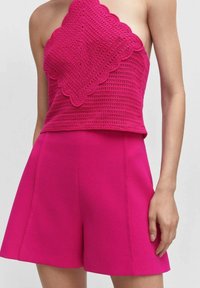Fuksjowy top na szydełku z falbaniastymi brzegami zestawiony z dopasowanymi szortami w kolorze fuksji. Stylizacja wyróżnia się teksturowanym materiałem i wyrafinowanym krojem.
