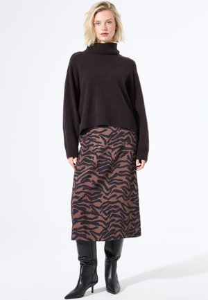 Bruine gebreide coltrui, cropped fit, gecombineerd met een midi-rok in bruine en zwarte tijgerprint en zwart leren laarzen tot de knie met hak.