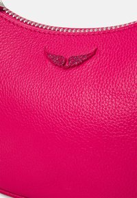 Sac en cuir texturé rose vif avec une fermeture éclair argentée et un petit logo en relief en forme d'aile près de la fermeture éclair.