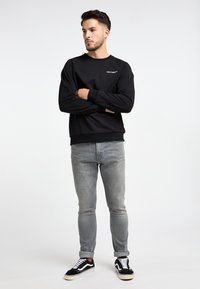 Felpa nera con polsini e orlo a coste, caratterizzata da un dettaglio logo bianco. Abbinata a jeans grigi a vita bassa e sneakers nere con accenti bianchi.
