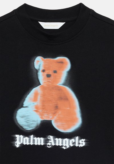 Μαύρο πουκάμισο με θολωμένο πορτοκαλί γραφικό αρκουδάκι και λευκό κείμενο "Palm Angels" σε γοτθική γραμματοσειρά κάτω από το αρκουδάκι.