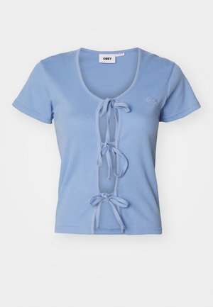 Vaaleansininen ribbed T-paita, jossa on lyhyet hihat, syvä V-pääntie ja etusiteet säätöä varten. Brändin nimi on brodeerattu rintaan.
