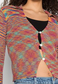 Multkleurige gebreide cardigan met een kraag, lange mouwen en een knoopsluiting aan de voorkant. Het levendige patroon bevat strepen in roze, blauw en geel.