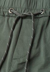 Short en tissu vert avec une taille élastique et un cordon gris passé dans des œillets métalliques.