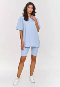 Jasnoniebieska, wygodna bluzka z krótkim rękawem w rozmiarze oversize, połączona z prążkowanymi, jasnoniebieskimi szortami rowerowymi, wykonanymi z miękkiego materiału. Całość dopełniają białe sneakersy.