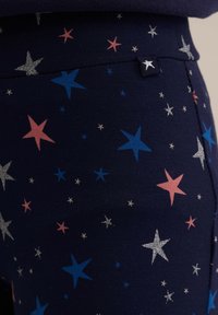 Mornarske leggins z zvezdastim vzorcem v roza, modri, srebrni in beli barvi. Narejeni so iz mehkega, raztegljivega materiala z subtilnim sijajem in šivanim detajlom.