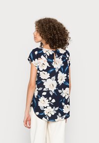 Top com padrão floral feito de tecido leve, fundo azul-marinho com flores brancas e rosa claro, apresentando um detalhe em buraco na parte de trás.