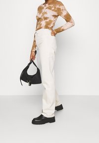 Jeans de pierna ancha blancos combinados con una blusa de manga larga marrón de estilo tie-dye, zapatos de plataforma negros y un pequeño bolso cruzado negro.