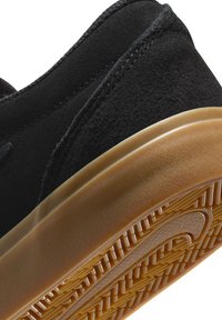 Zapatilla de ante negra con un upper texturizado, que presenta una suela exterior de goma con un dibujo en la banda de rodadura y un logo visible en el lateral.