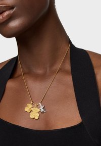 Collana con pendente in oro e argento, caratterizzata da tre ciondoli a forma di foglia, con dettagli texture e una delicata catena di perline.