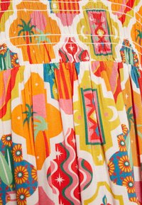 Farverigt stof med et levende, geometrisk mønster i røde, orange, lyserøde og grønne nuancer; struktureret smock-effekt i toppen.