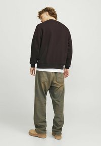 Donkerbruin sweatshirt van katoen, relaxed fit. Olijfgroene, losvallende jeans met een vervaagde textuur. Tan laarzen. Neutrale achtergrond.
