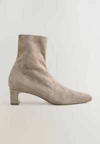 Beige mokasini niloni mguu kwa kidole kilichopigwa, na kisigino cha chini chenye mchanganyiko wa uso laini. Ina vipengele vya kushona kwenye pande zake.