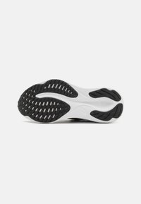 Semelle de chaussure de sport en noir et blanc présentant une surface en caoutchouc texturée avec de multiples motifs de traction et un talon renforcé.