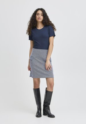 Top navy cu dungi, asortat cu o fustă texturată bleu, ce dispune de un buzunar lateral. Modelul poartă cizme negre înalte pentru contrast. Design simplu și modern.