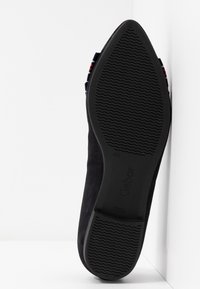 Chaussure en suede noir avec une semelle en caoutchouc texturée à motif ondulé, présentant un design à profil bas et une petite sangle d'accent à l'arrière.