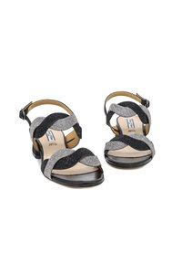 Sandali neri e argento con cinturini ondulati realizzati in tessuto testurizzato e pelle. Design con punta aperta, tacco basso e cinturino alla caviglia regolabile.