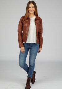 Bruine leren jas met een aansluitend ontwerp, twee voorzakken en een ritssluiting, gecombineerd met lichtblauwe skinny jeans en bruine veterschoenen.