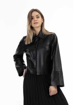 Black leather cropped jacket with a collared neckline, button closure, and flared sleeves, paired with a pleated black skirt.