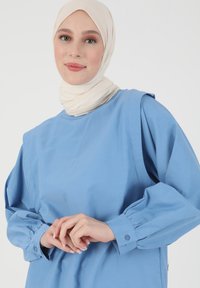 Blusa azzurro chiaro con scollo rotondo e maniche a sbuffo. Presenta polsini con bottoni e un tessuto leggero e morbido.